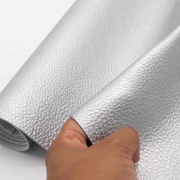 A close-up of a hand holding a roll of metallic silver textured material, showing its pebbled leather-like surface against a plain white background.