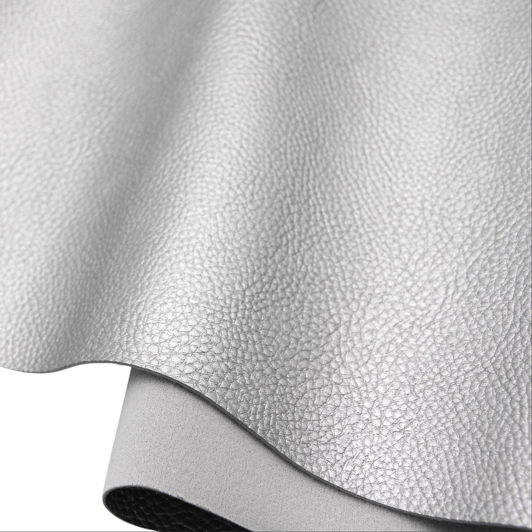 A close-up of a light gray pebbled faux leather or vinyl material sheet, partially rolled over to show its texture and underside on a white background.