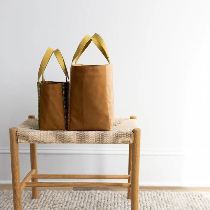 Two brown bags with yellow handles on a wooden chair against a white wall.