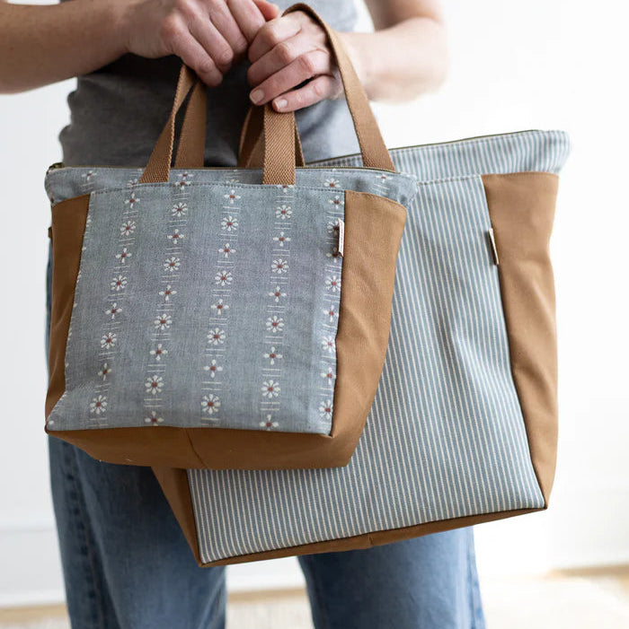 Person holding a tote bag with a floral pattern on a neutral background