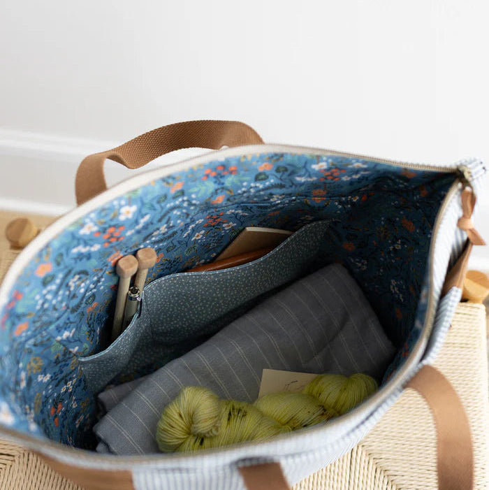 Open bag with floral pattern and yarn inside on a light wooden surface.